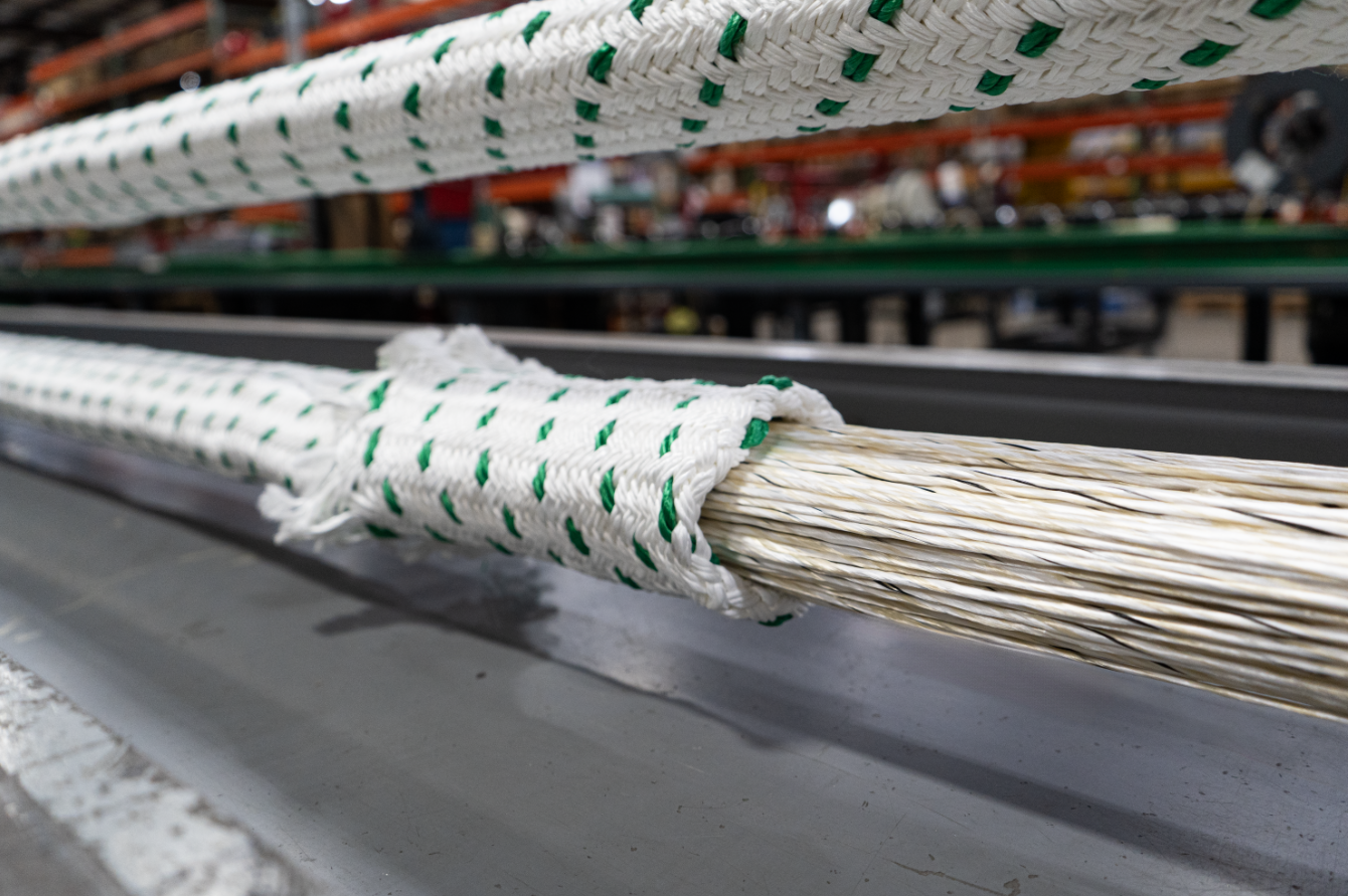 Close-up of braided white rope with green threads resting on a gray metal surface in a workshop/industrial setting.